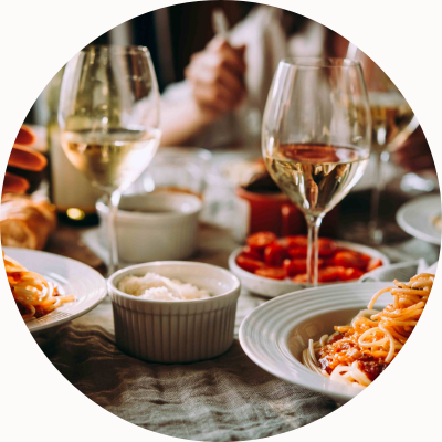 A plate of pasta with glasses of wine on a table and a person in the background.