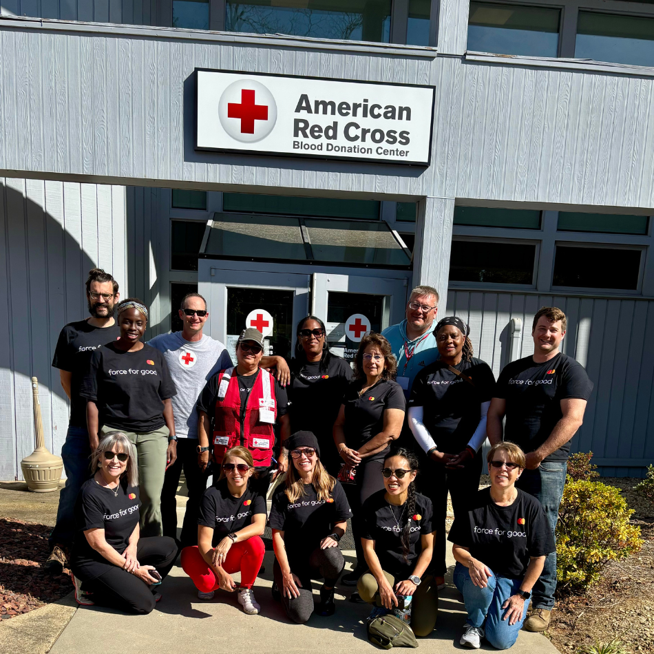 Mastercard employees deployed to the Red Cross's community care center in North Carolina pose in front of a building with a Red Cross sign. 