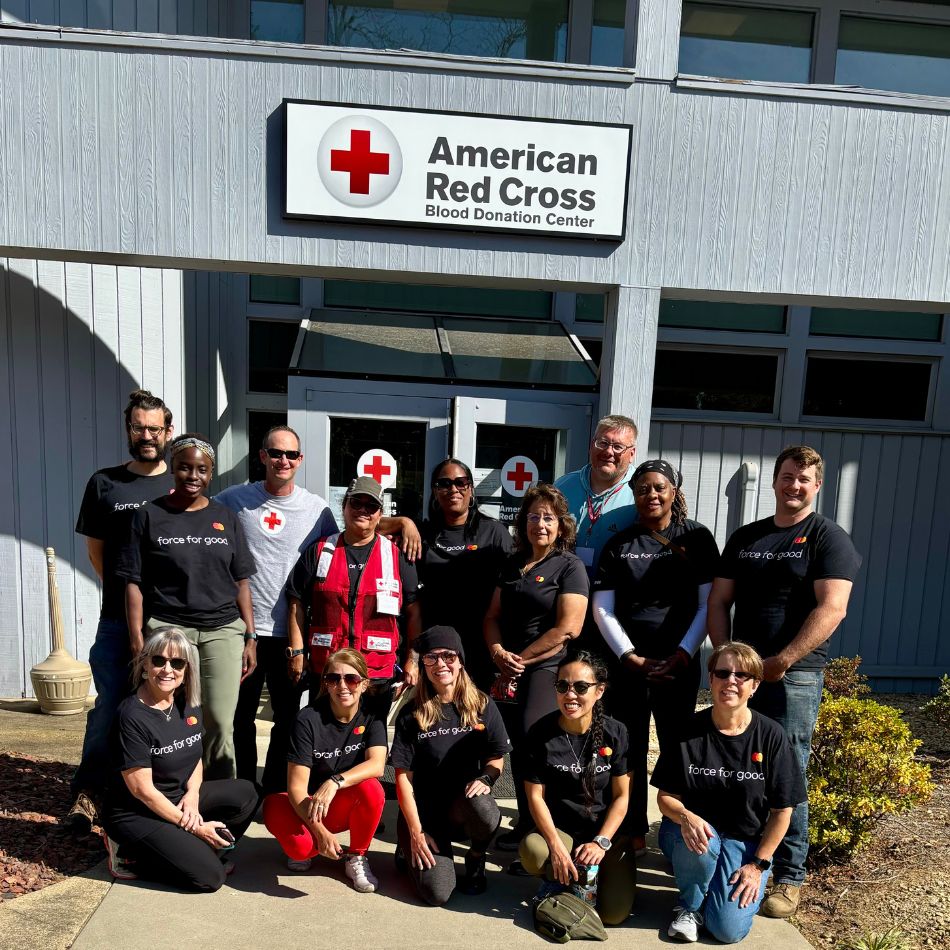 Mastercard employees deployed to the Red Cross's community care center in North Carolina pose in front of a building with a Red Cross sign.