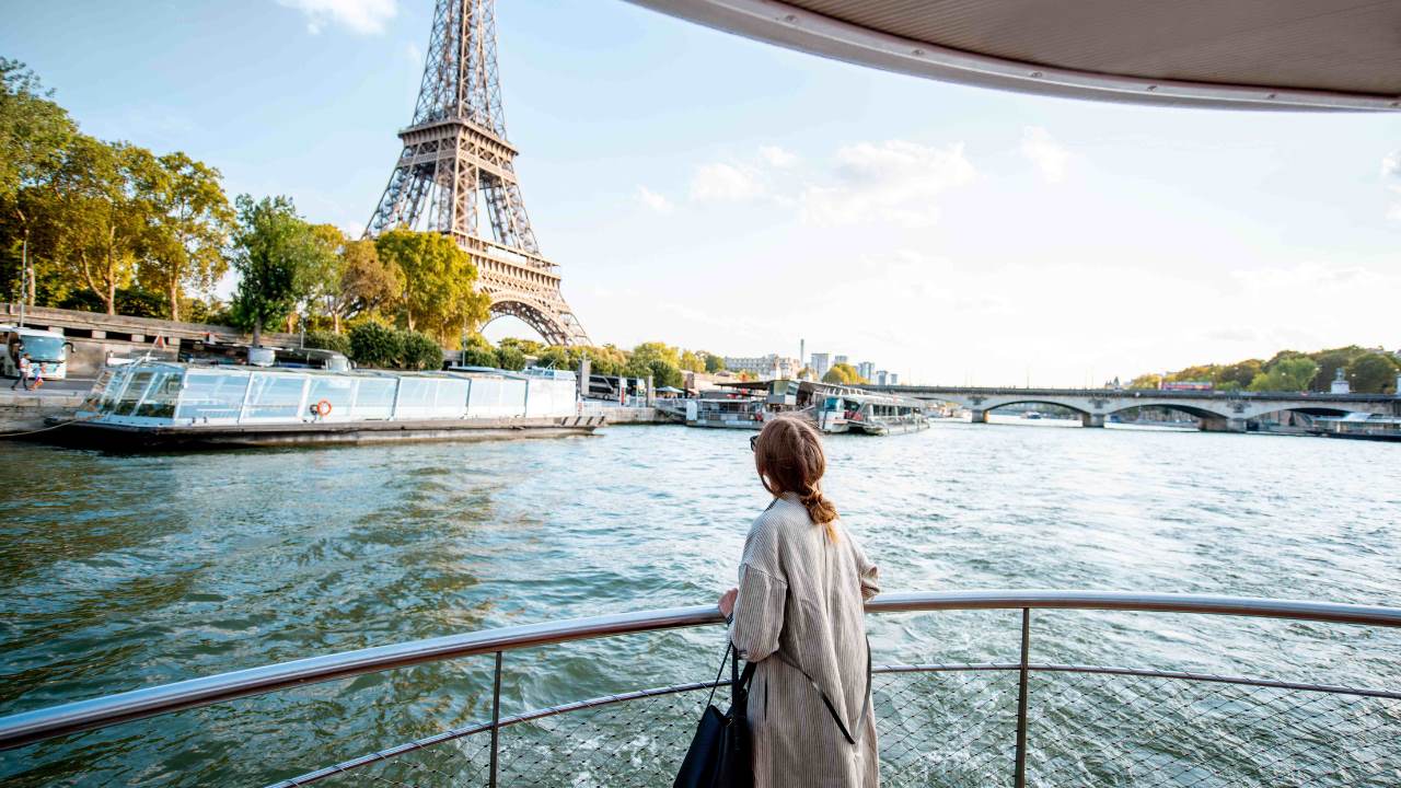 A woman stands at the railing of a boat as it passes by the Eiffel Tower.