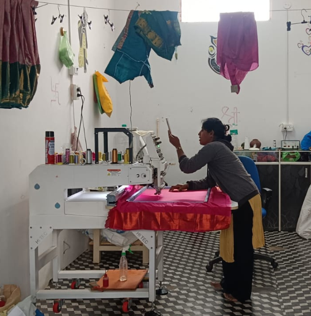 An Indian woman in a fabric embroidery shop takes a photo of her work. 