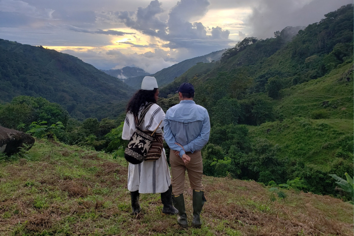 Two men, one in traditional Arhuaco dress, stand on a mountain in the Sierra Nevada de Santa Martas in Colombia. 