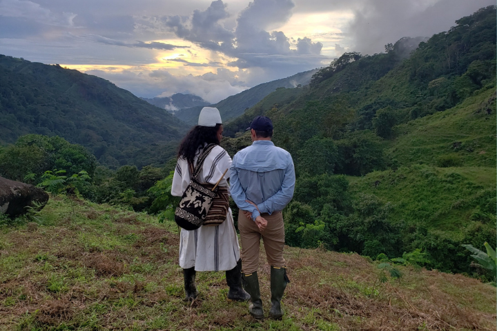 Two men, one in traditional Arhuaco dress, stand on a mountain in the Sierra Nevada de Santa Martas in Colombia.