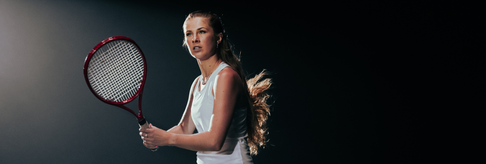 Courtney Webeck, a low-vision tennis champion, holds a tennis racquet in front of a black background.