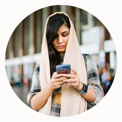 A woman wearing a scarf around her head looks at a smartphone.