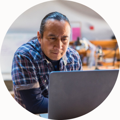 A man in a plaid shirt in a workshop looks at his laptop.