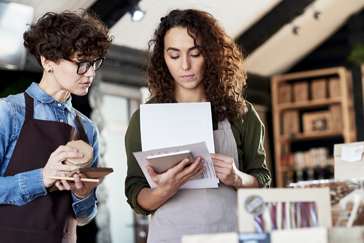 A worker looks at paperwork while another holds a writing implement and looks on.