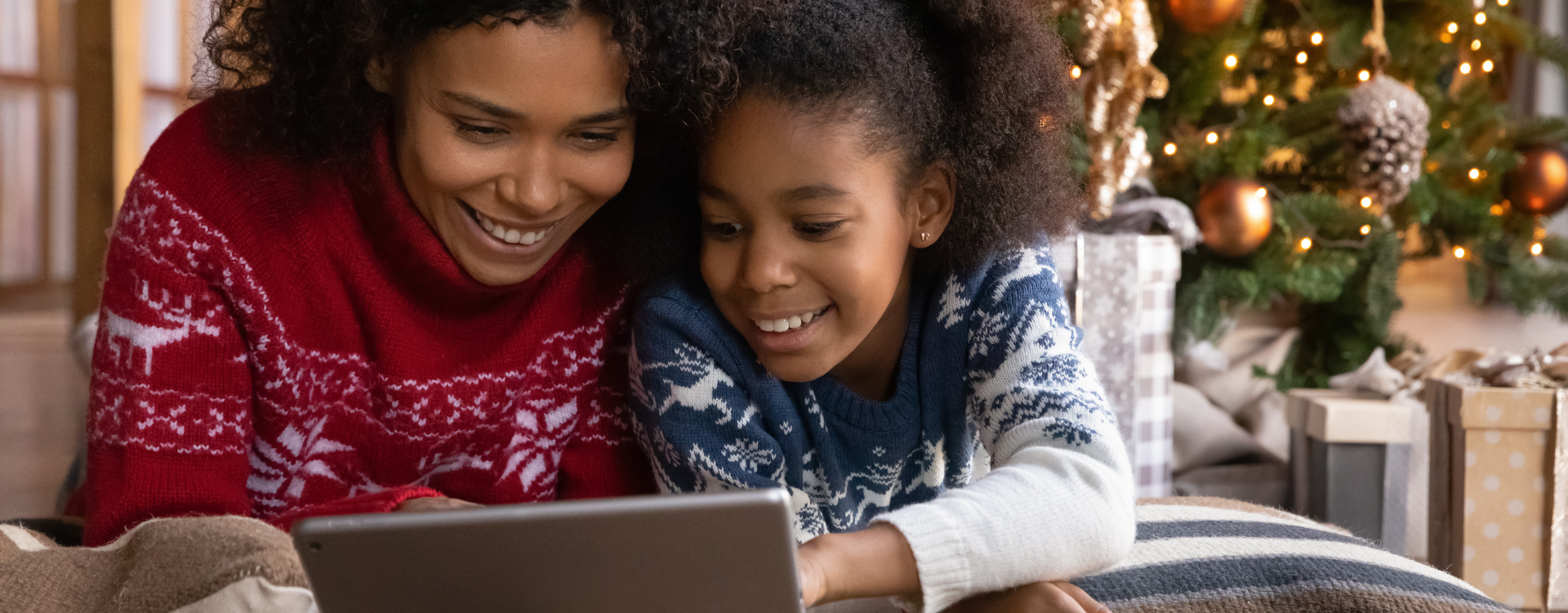 A mother and daugher look at a tablet with a Christmas tree in the background. 