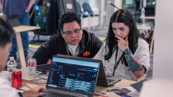 Two cybersecurity experts look at a laptop.