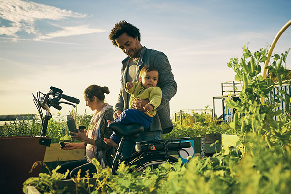 A man holds a baby at a farm stand while another child walks next to him.