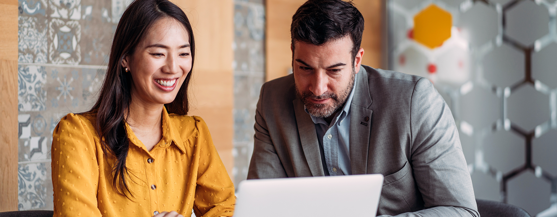 A woman and a man look at a laptop in an office.