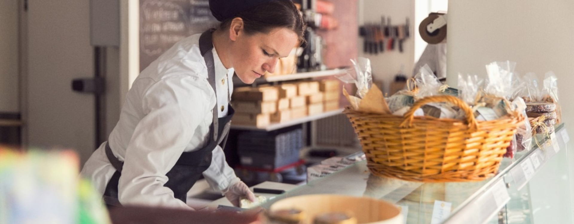 A woman in an apron writes on a counter in a bakery.