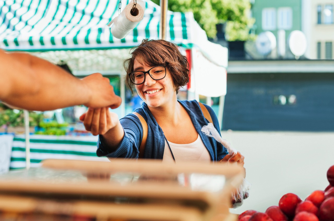 A woman pays for a purchase at a fruit stand. 