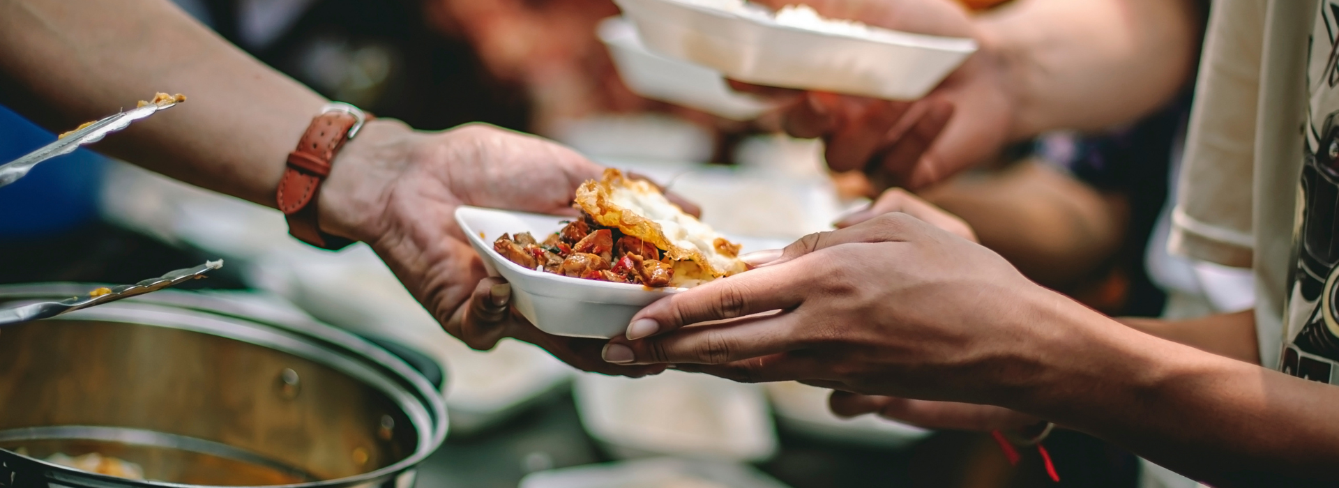 A person hands a plate of food to someone at a soup kitchen. 