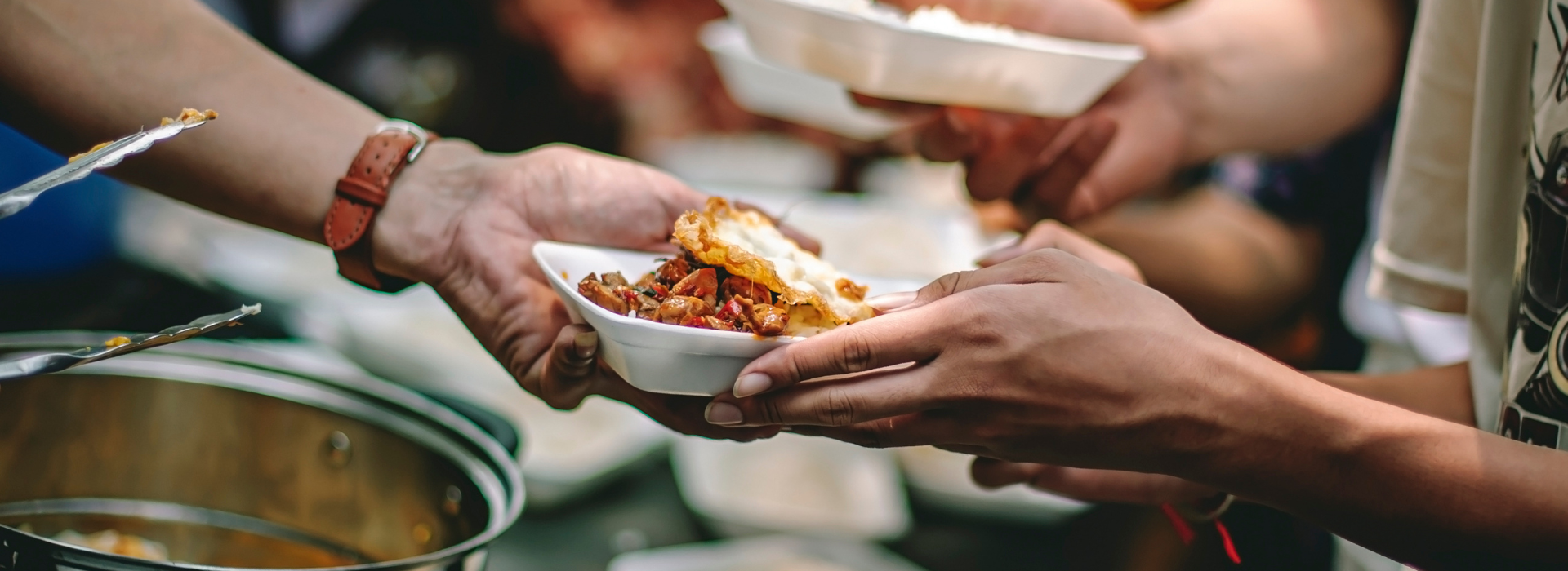 A person hands a plate of food to someone at a soup kitchen.