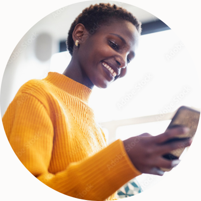 A woman in a yellow sweater smiles at her smartphone.