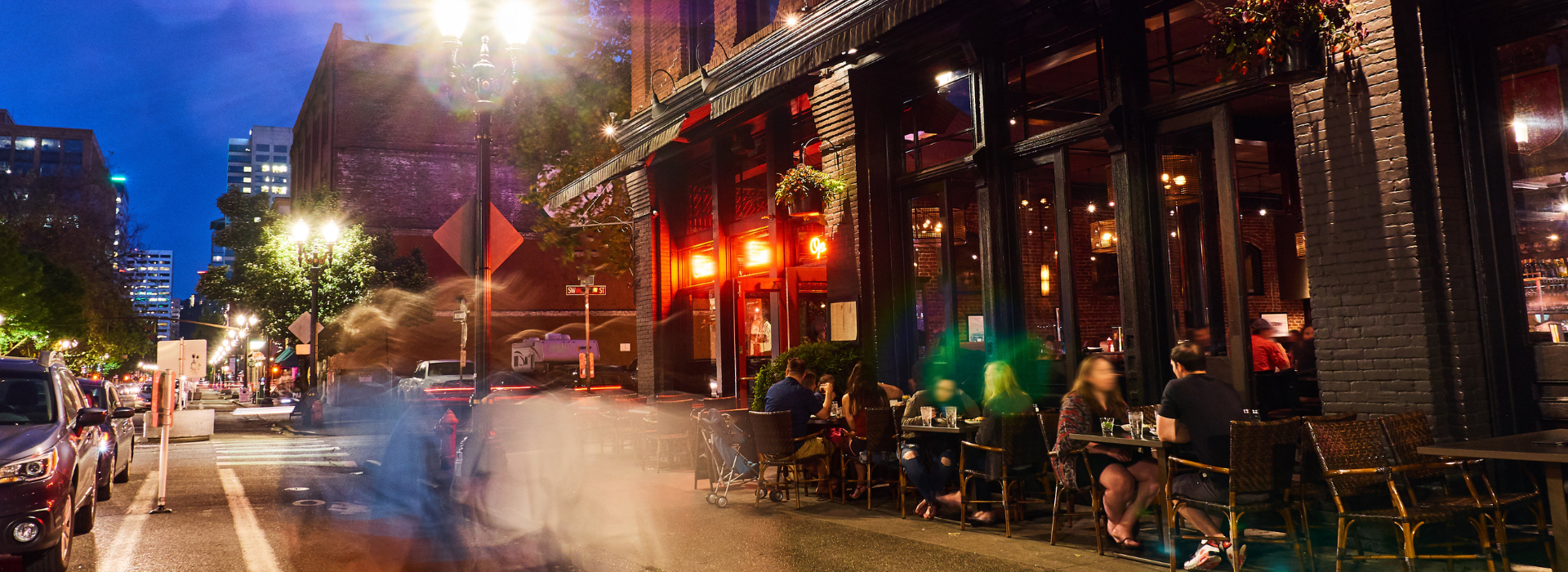 Street scene of New York City with people eating at a sidewalk restaurant at night. 