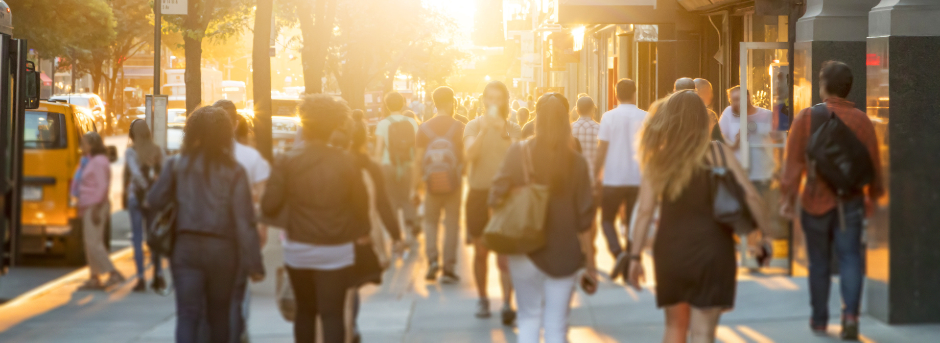 People walking through a busy downtown district as the sun is setting.