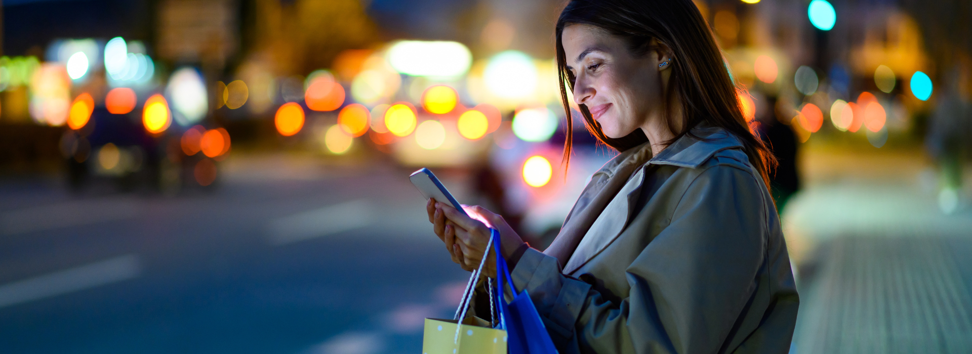 A woman with shopping bags looks at her phone near a busy street. 