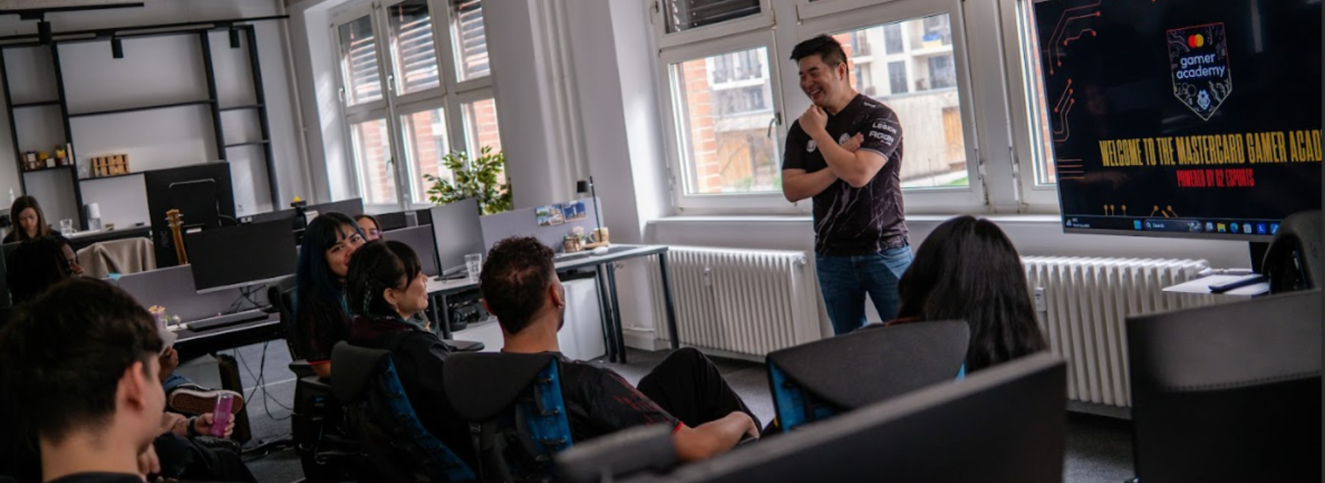 Members of the Mastercard Gamer Academy speaks with a G2 representative in an office setting in front of a screen.