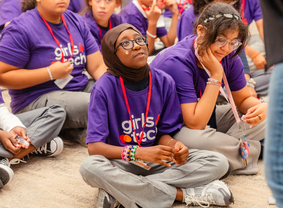 A young girl in a head scarf and a Girls4Tech T-shirt listens to a presentation at a cyber and AI event at the Mastercard Tech Hub in Manhattan.